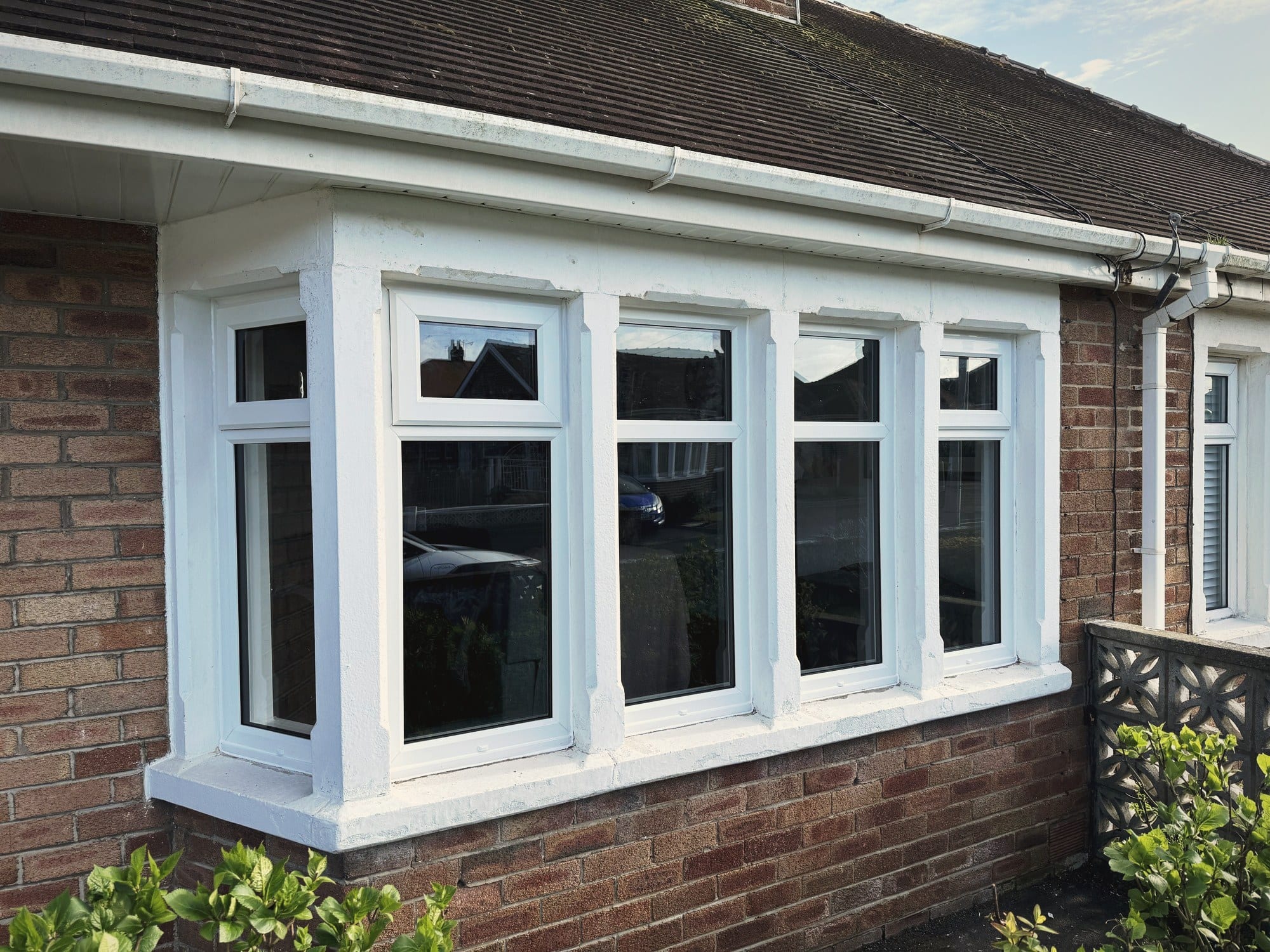 A white uPVC bay window with four lights, fitted into a rendered bungalow above a brick sill