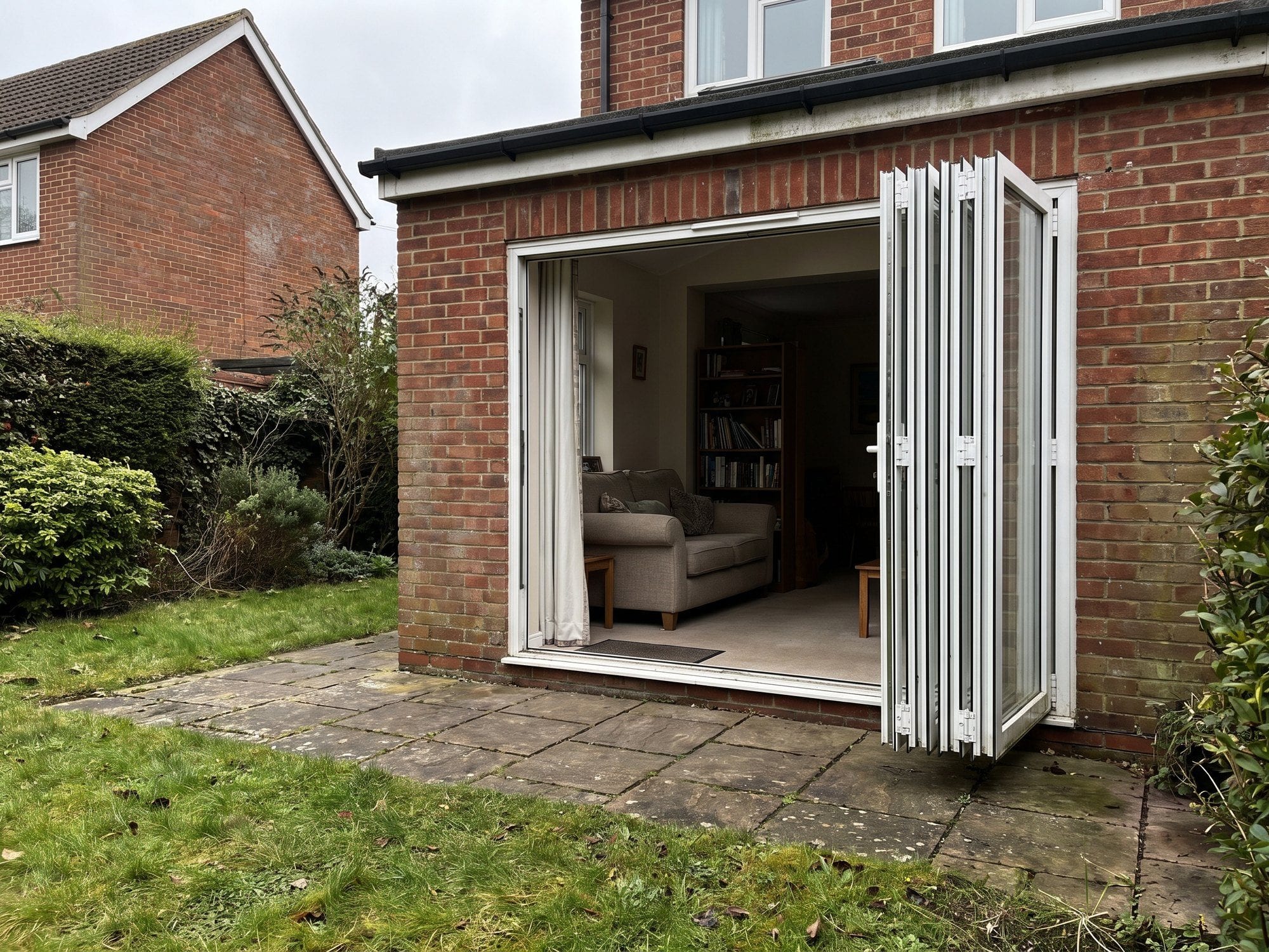 White bi-fold doors folded fully open on the rear of a brick house, looking in from a paved patio
