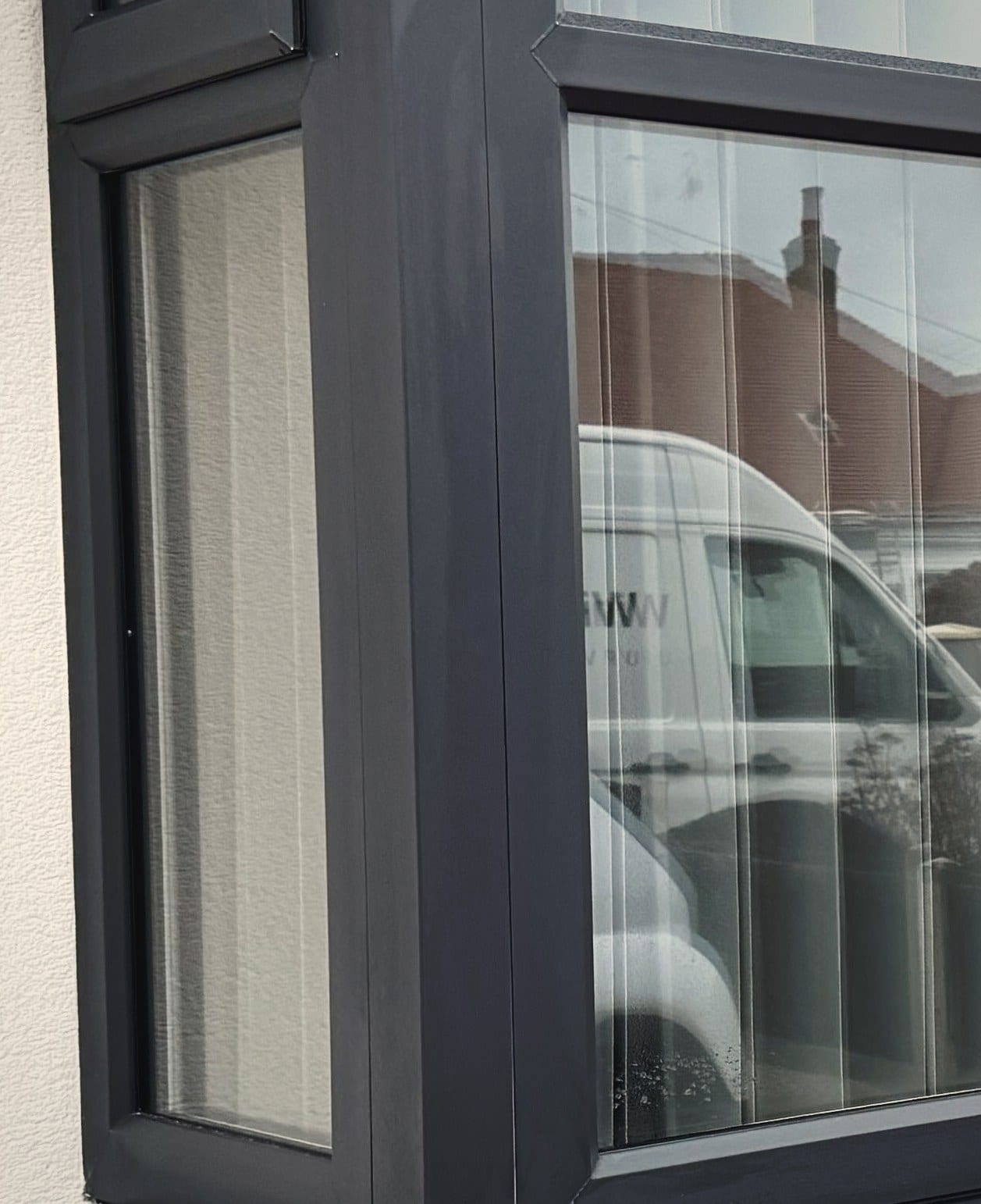 Close view of the corner of a uPVC bay window, showing the mullion, the sealed unit edge and the frame junction behind it