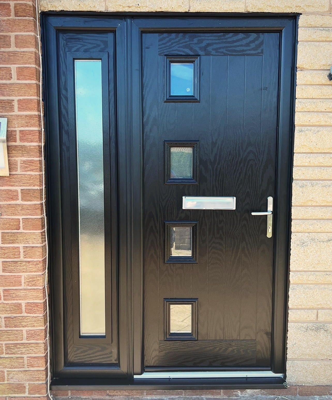 An anthracite composite front door with a long glazed side panel, fitted into a stone and brick surround