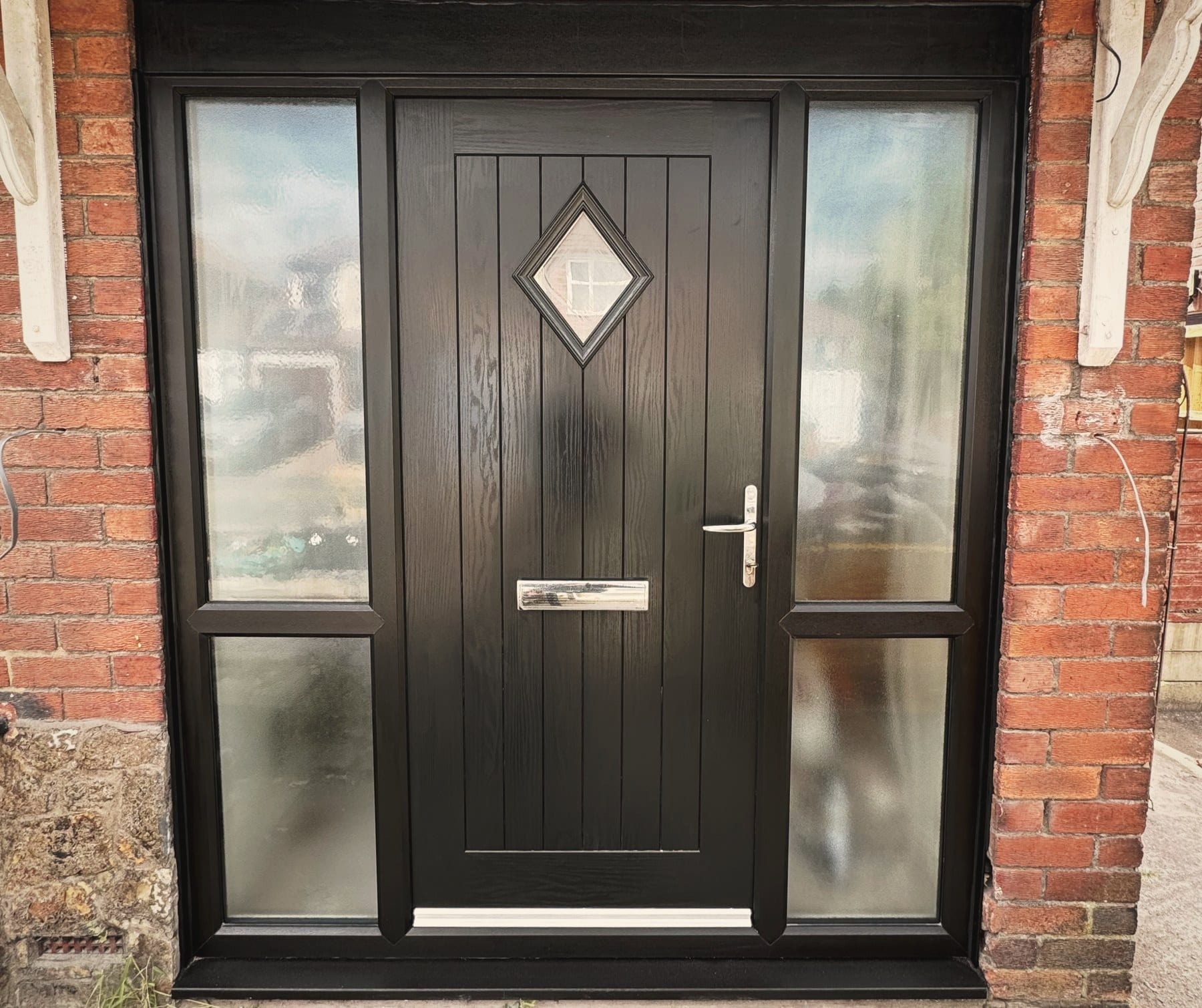 A black composite front door with a diamond glazed panel and long glazed side light, in a stone surround