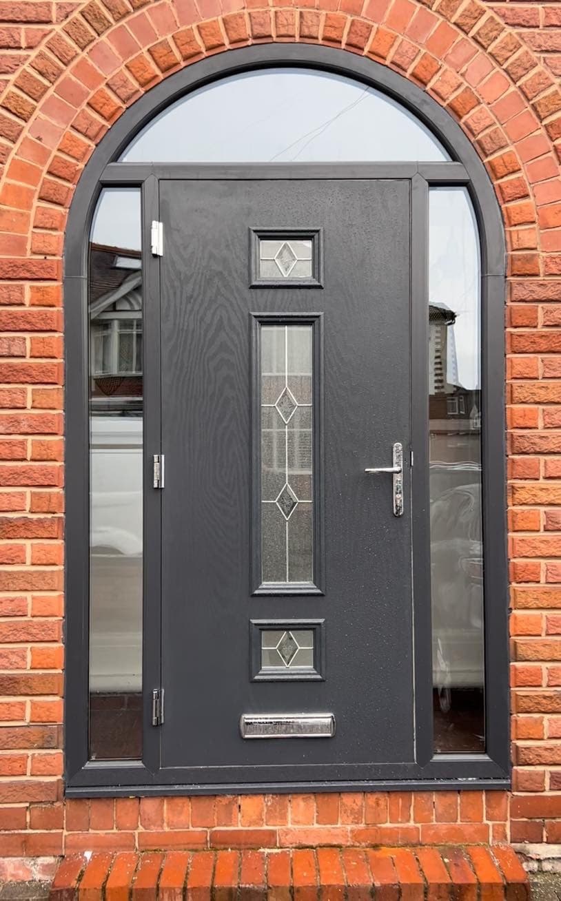 A grey composite front door with diamond glazing and a glazed side panel, set in a red brick arch