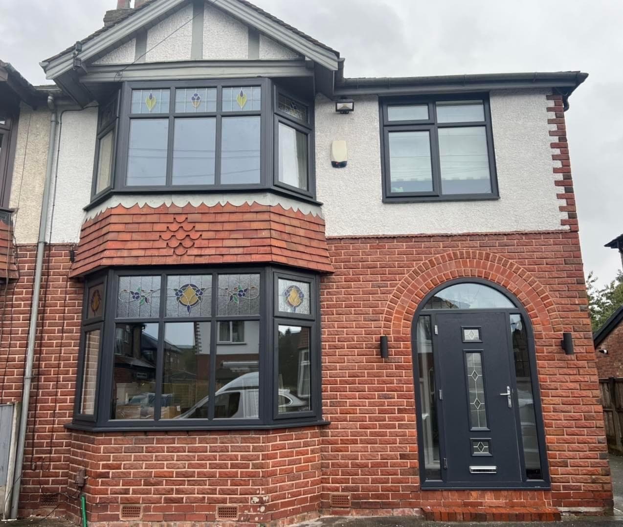A brick and render semi with a leaded and stained glass bay window and an arched anthracite composite door