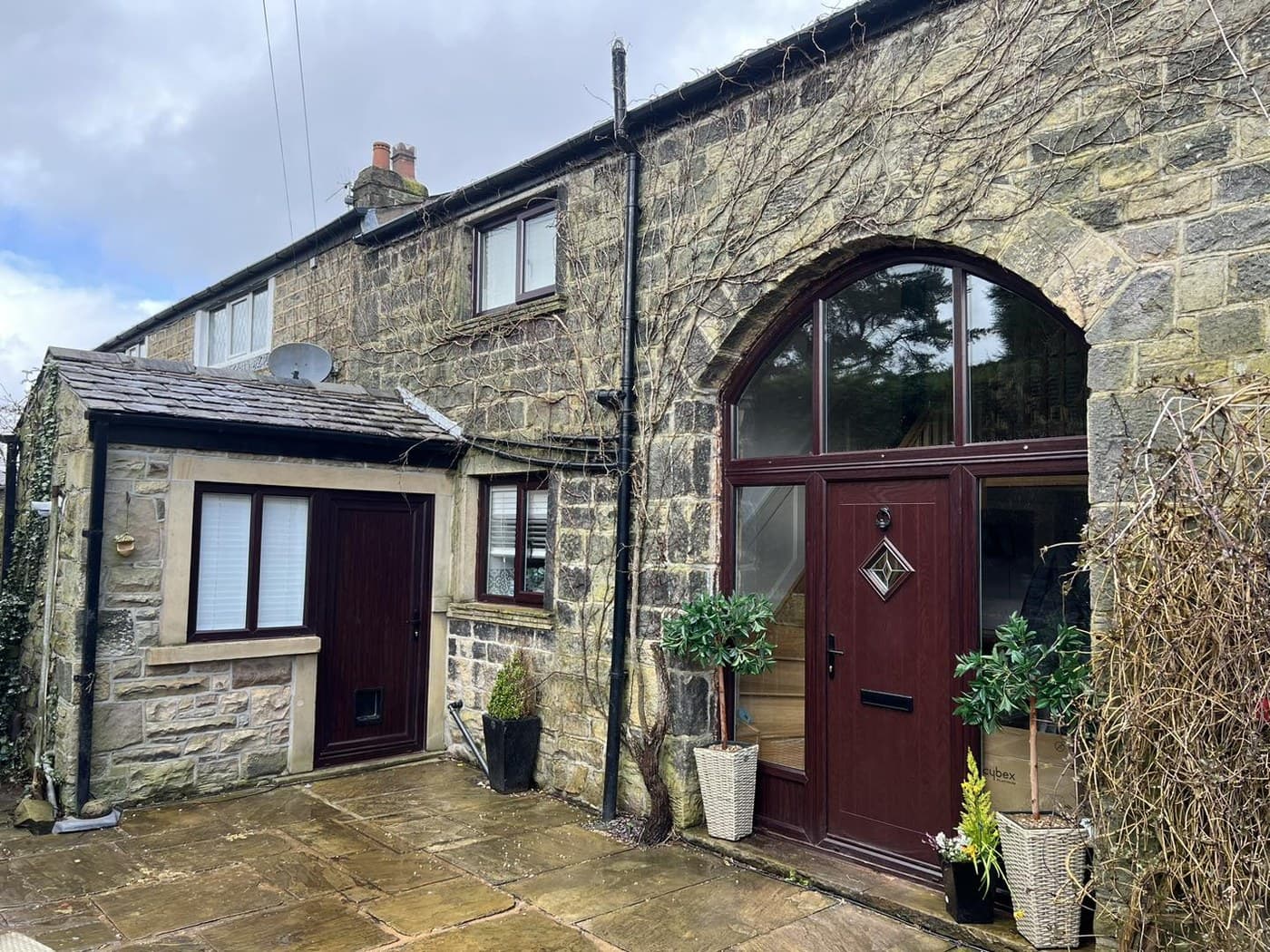 A stone cottage with an arched dark red composite front door