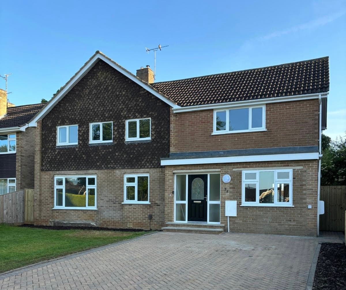 A 1970s detached house with white uPVC windows throughout and a block paved drive