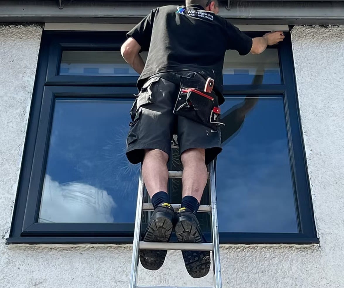 A fitter on a ladder, sealing the head of a newly fitted window
