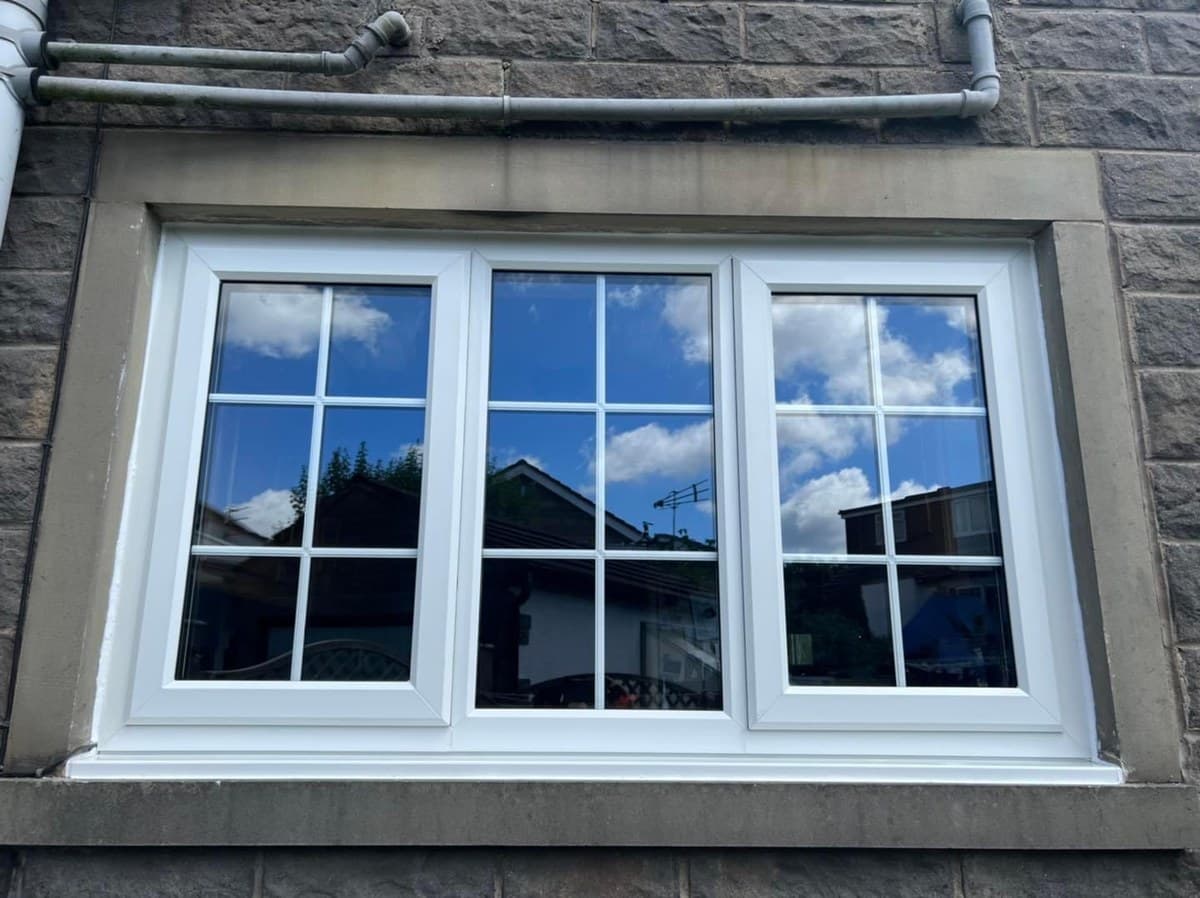 A white uPVC window with Georgian bars, fitted into a stone reveal