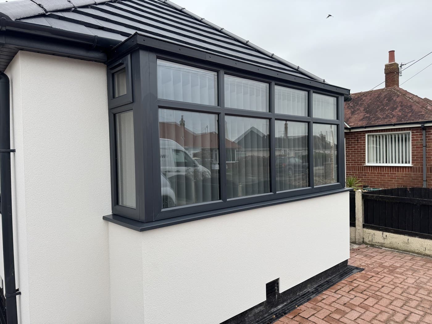 An anthracite framed lean to orangery on a white rendered extension