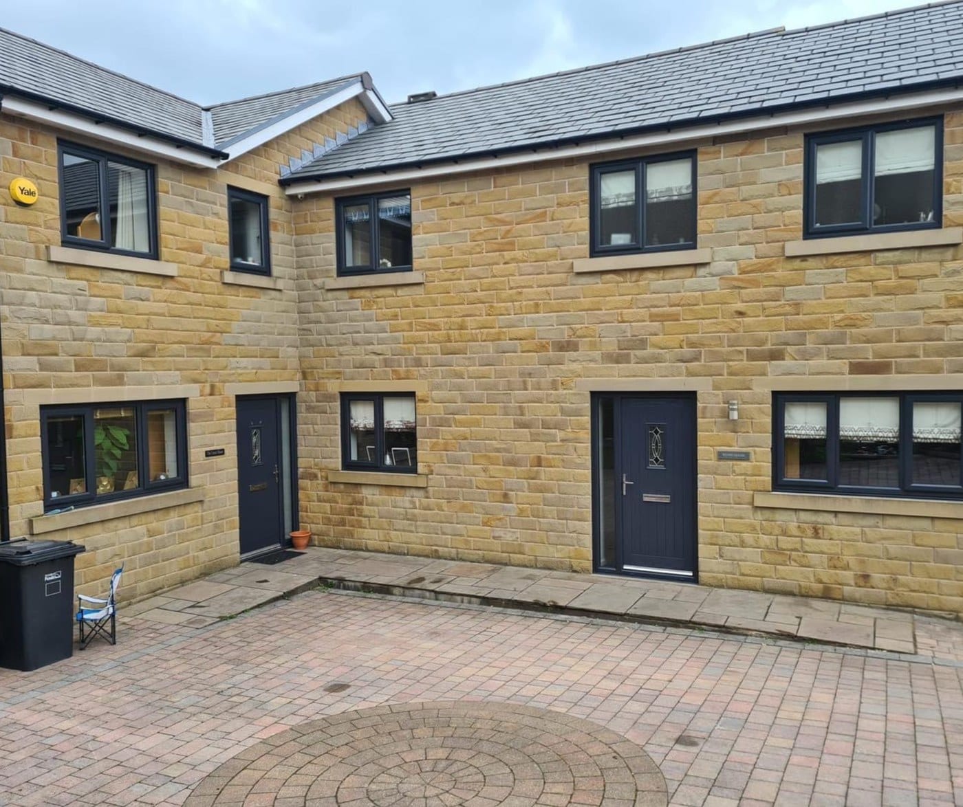 A pair of modern stone built semi detached houses with grey uPVC windows and dark composite front doors
