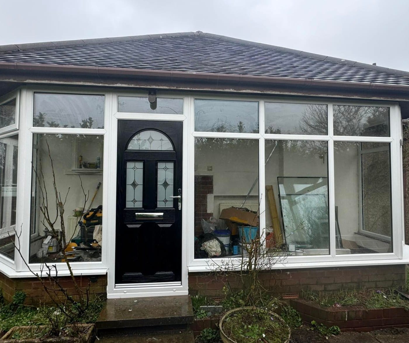 After: the same sunroom with white uPVC frames throughout and a black composite door with diamond glazing