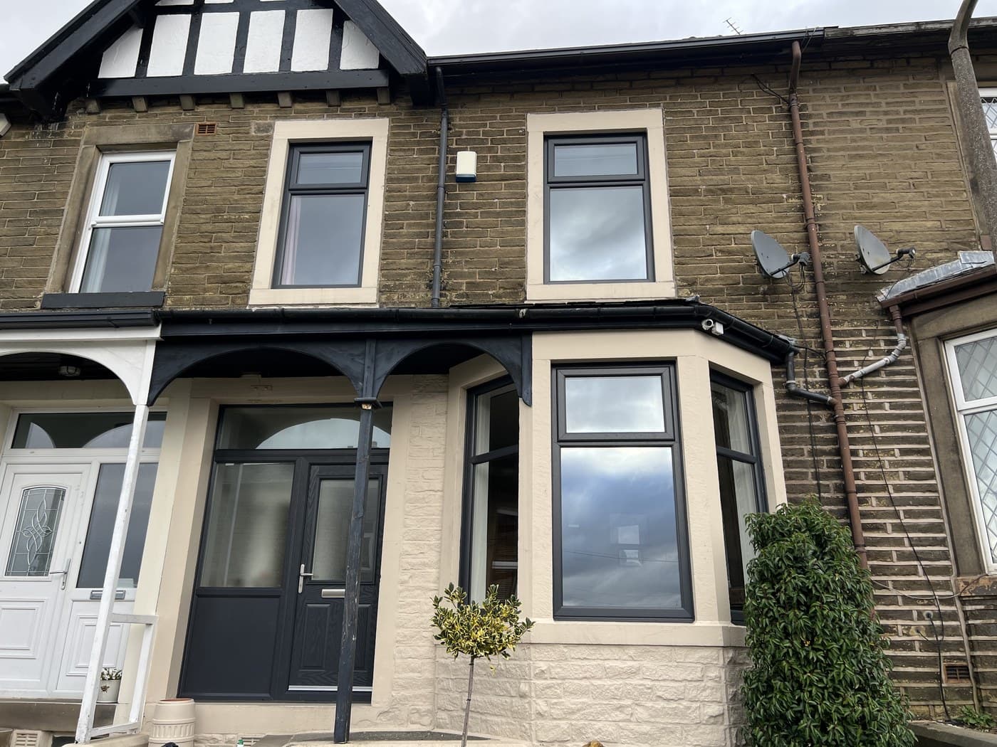 A stone terrace with new uPVC bay windows and a dark composite door under a timber porch