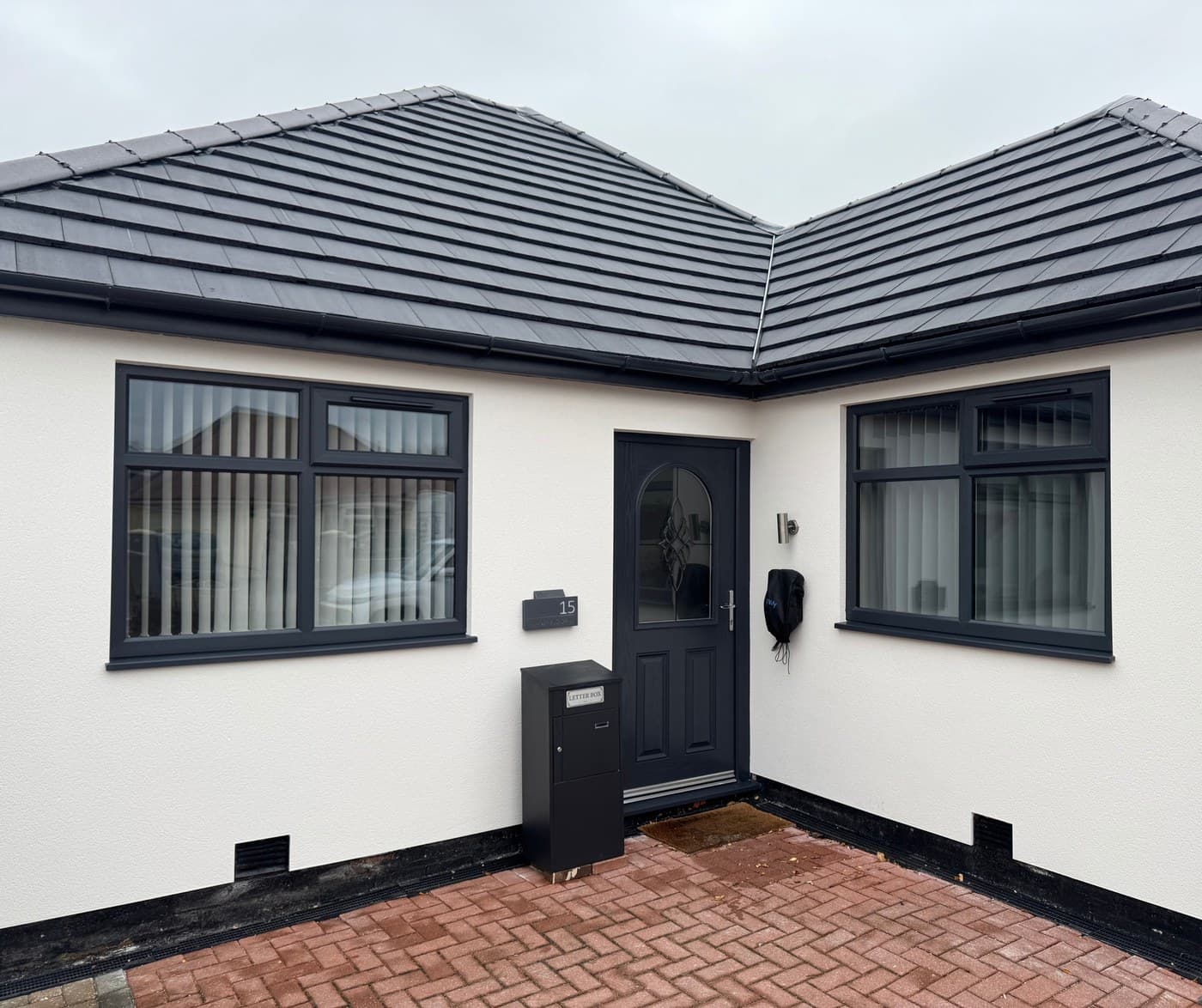 A white rendered bungalow with anthracite uPVC windows and a dark composite front door