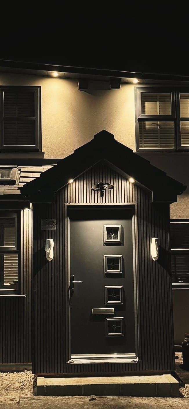 A detached house at dusk with a lit porch, an anthracite composite front door and matching dark window frames