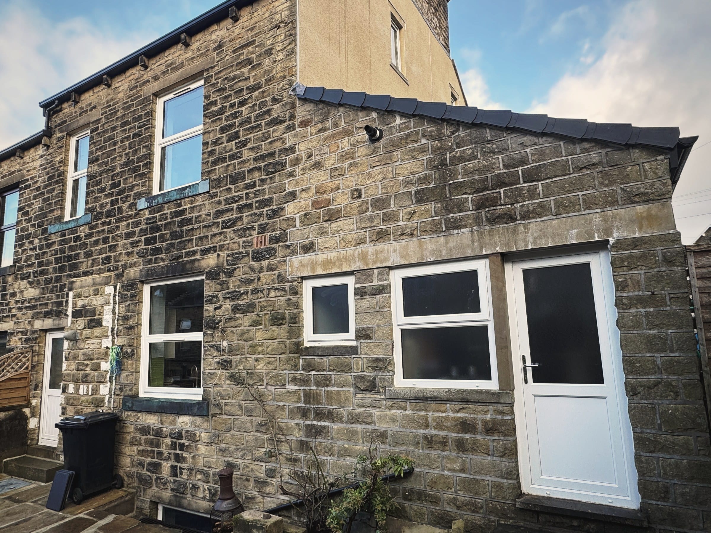 The rear of a gritstone house with a white uPVC side access door and replacement windows
