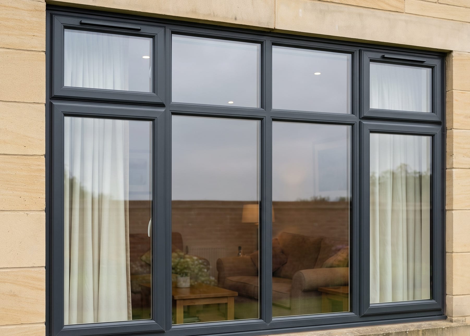 An anthracite grey uPVC window in the sandstone wall of a house, with the lounge visible through the glass